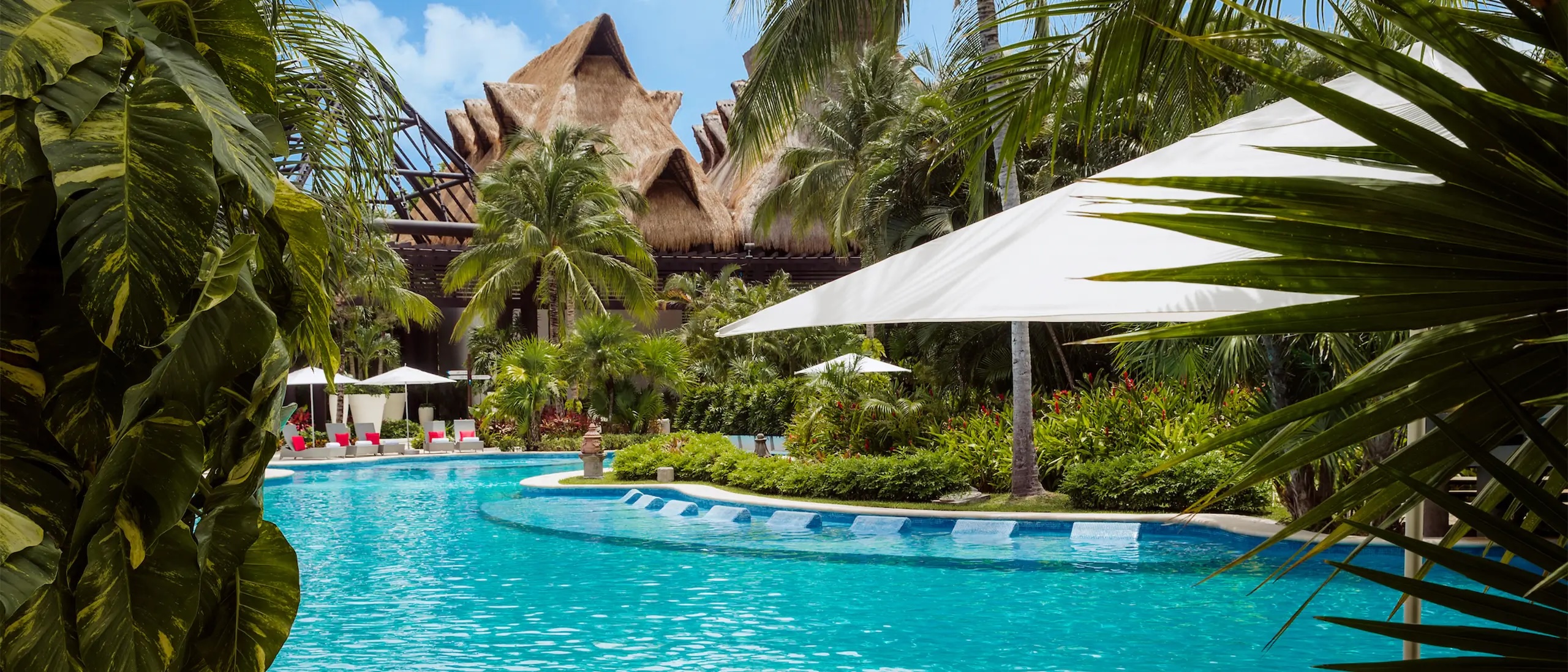 Vista de la alberca y jardín tropical de Vidanta Riviera Maya, con palapas tradicionales y vegetación exuberante